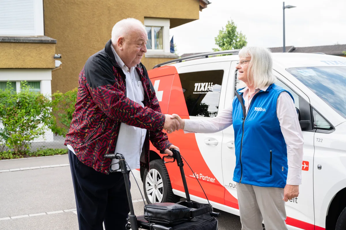 Ein Mann mit Rollator gibt einer Frau die Hand. 